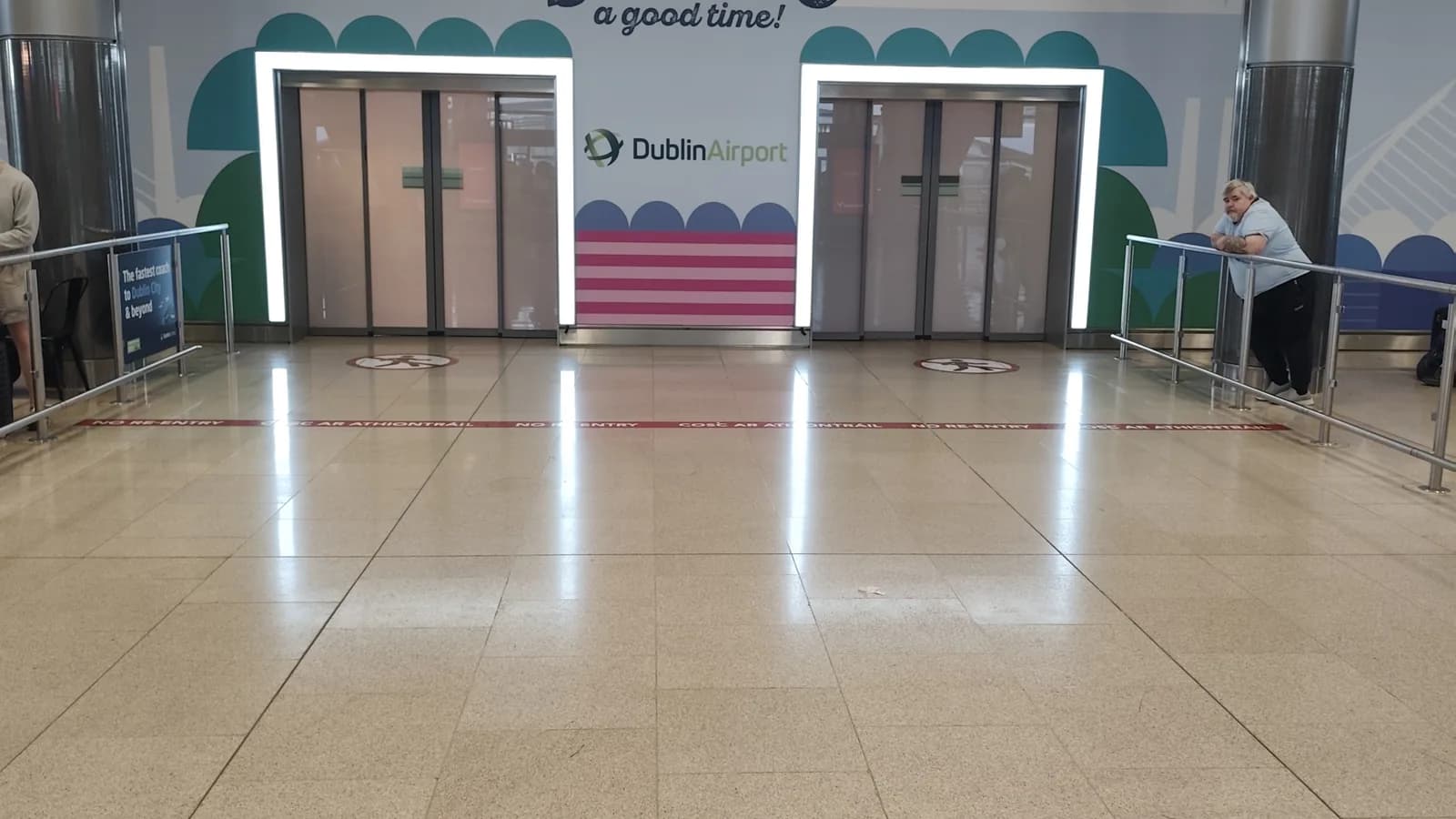 The sliding exit doors from baggage reclaim into the public arrivals hall at Dublin Airport, with the red no re-entry line on the floor where drivers wait for arriving passengers