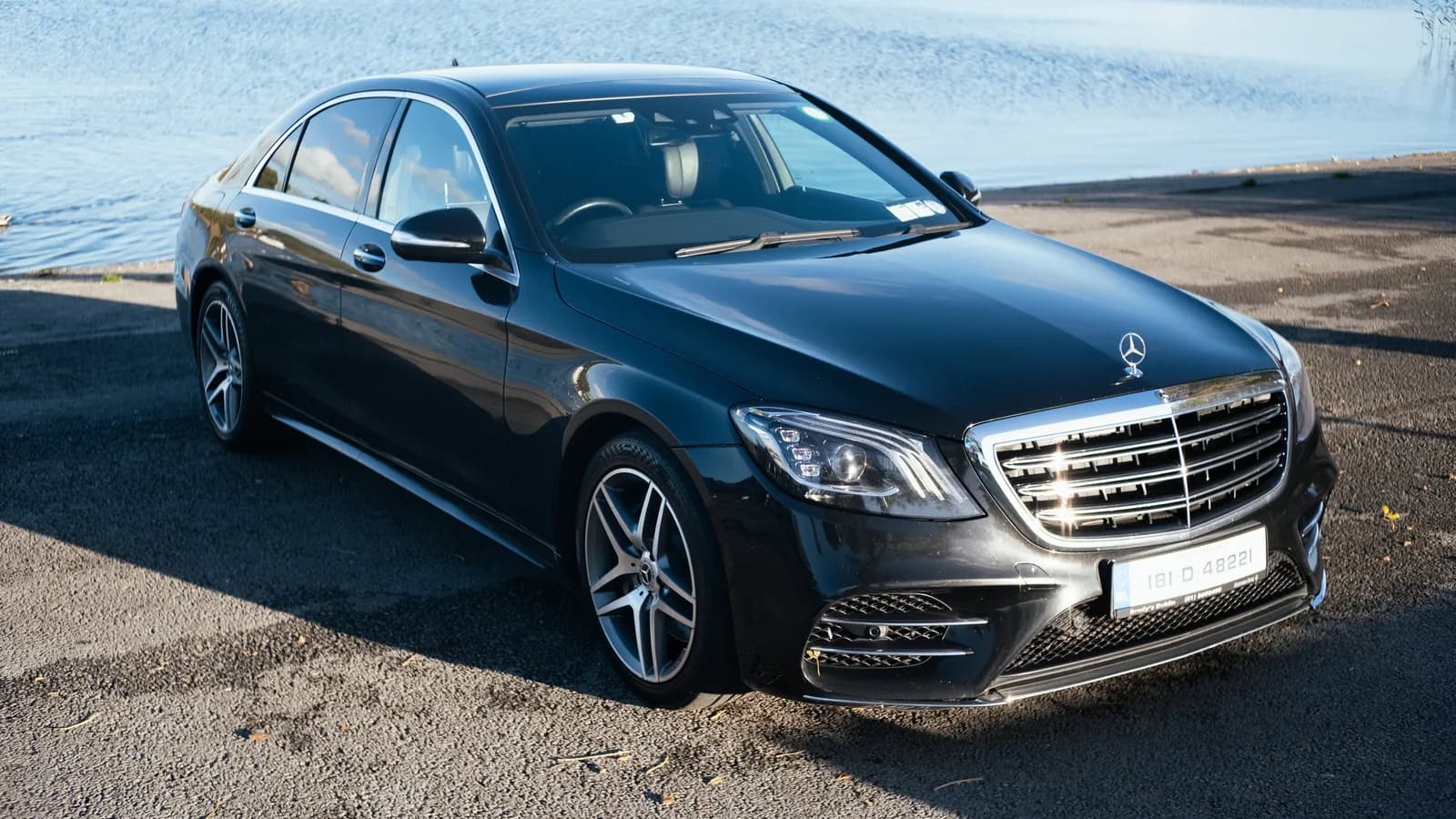 Black Mercedes-Benz S-Class parked beside a lake on a sunny day