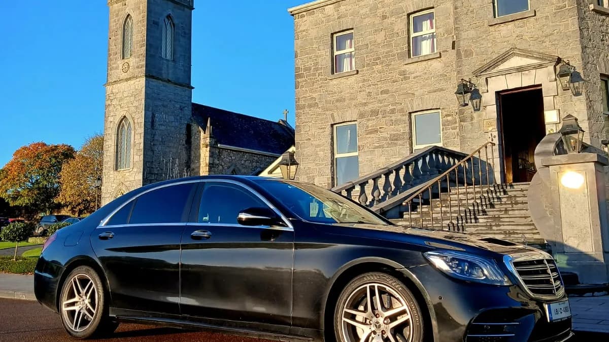 Black Mercedes-Benz S-Class parked outside a stone country house beside a church tower
