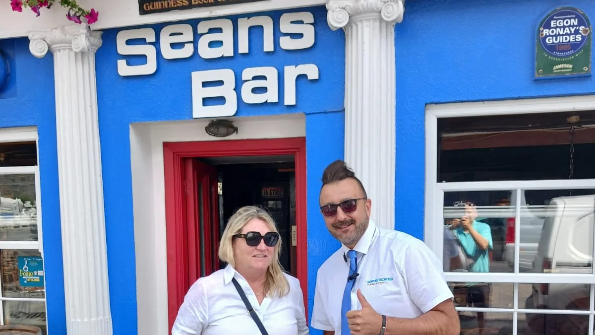 A guest and her Sophisticated Travels & Tours chauffeur standing outside the blue front and red door of Sean's Bar in Athlone during a private heritage tour